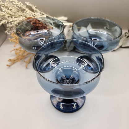 Set of three smoky blue glass dessert coupes with short stems and rounded bowls.