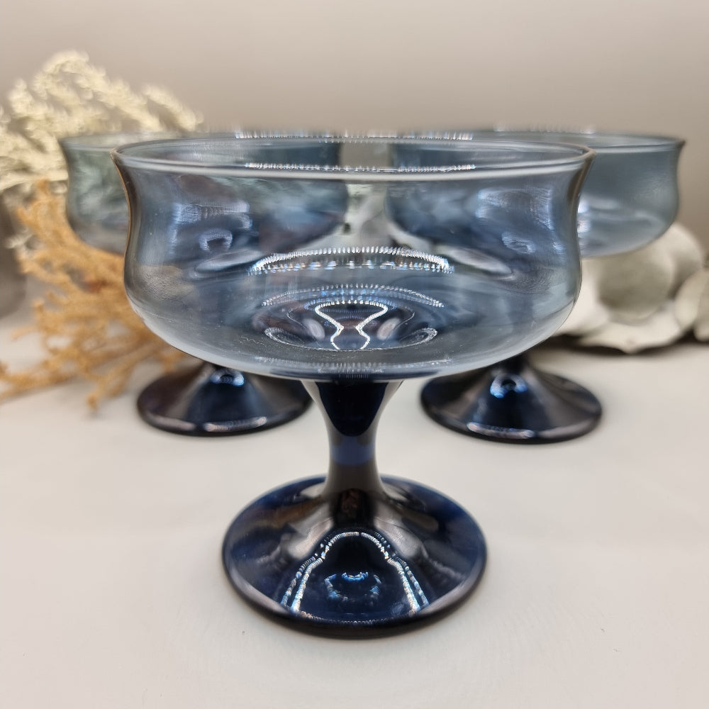 Set of three smoky blue glass dessert coupes with short stems and rounded bowls.