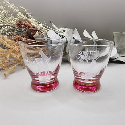 Pair of etched cranberry glass liqueur glasses with floral engravings and pink bases.