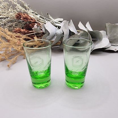 Pair of etched green glass shot glasses with clear tops and vibrant green bases.