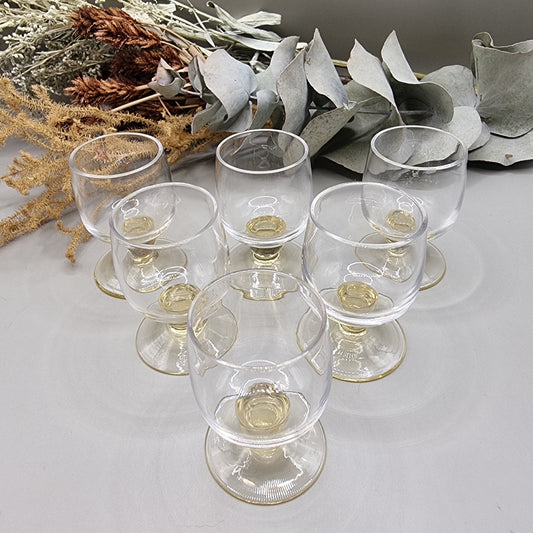 Set of six yellow-tinted vintage shot glasses with rounded bowls and short pedestal bases.
