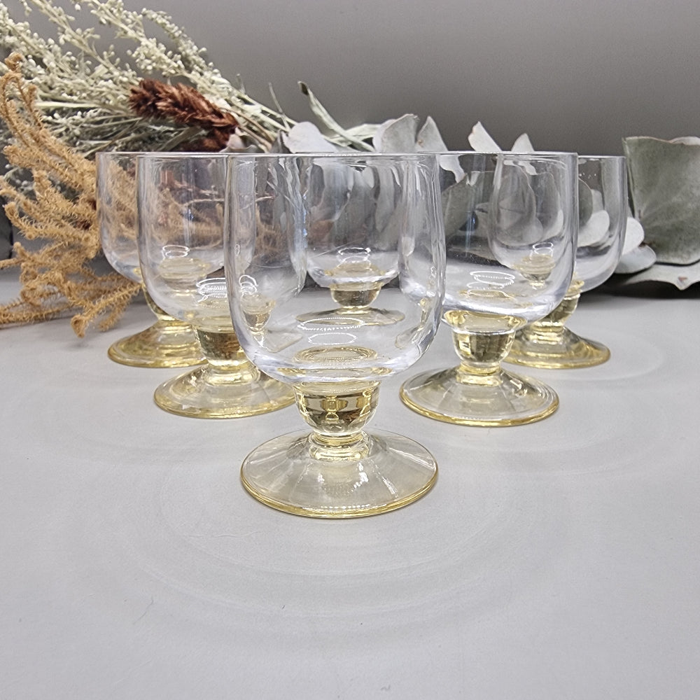 Set of six yellow-tinted vintage shot glasses with rounded bowls and short pedestal bases.