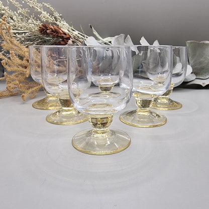 Set of six yellow-tinted vintage shot glasses with rounded bowls and short pedestal bases.