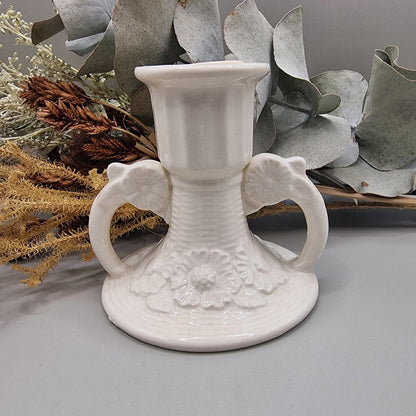 White ceramic twin handle candle holder with raised floral base detail and glossy glaze.