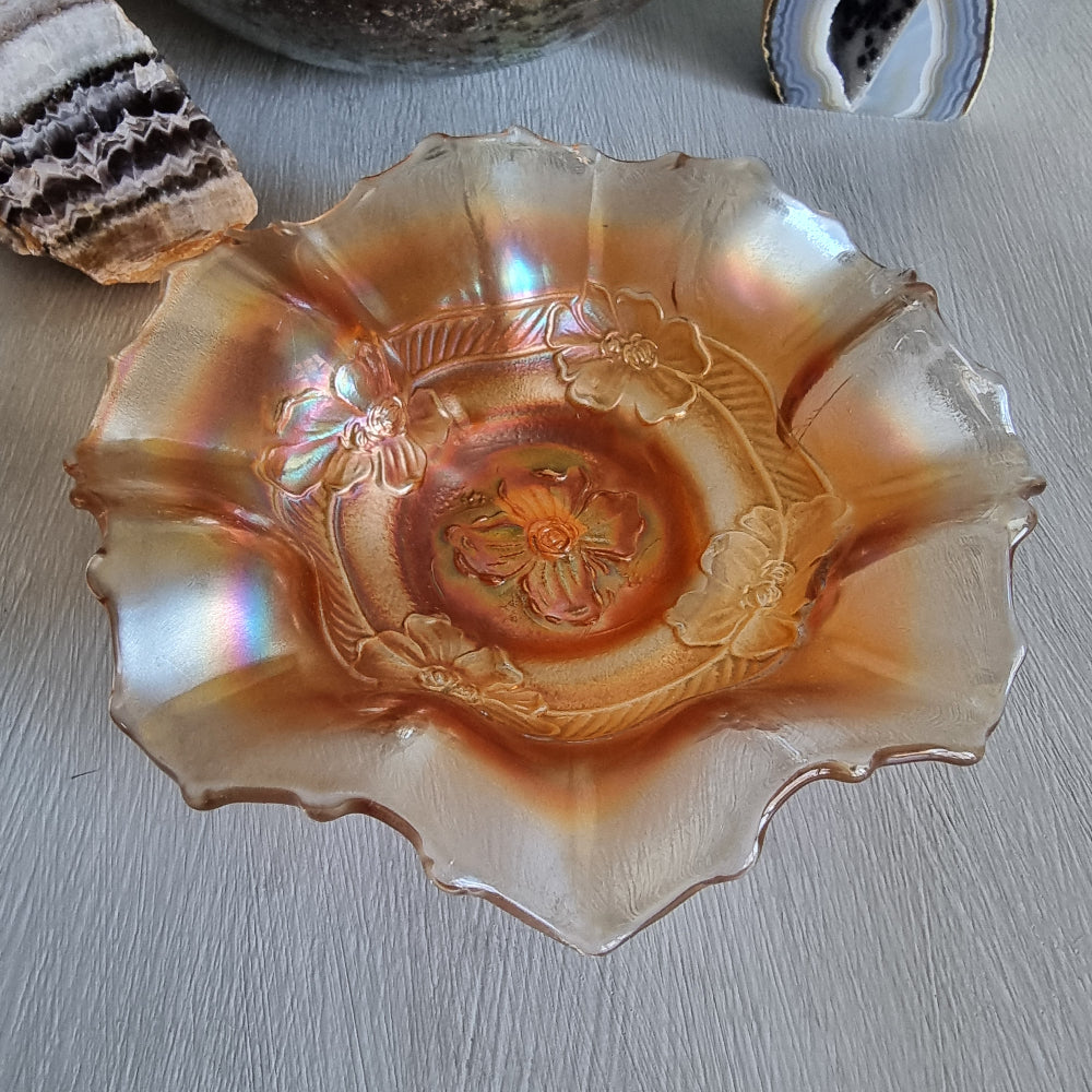 Vintage carnival glass bowl with ruffled edge and embossed floral pattern in peach-gold tones.