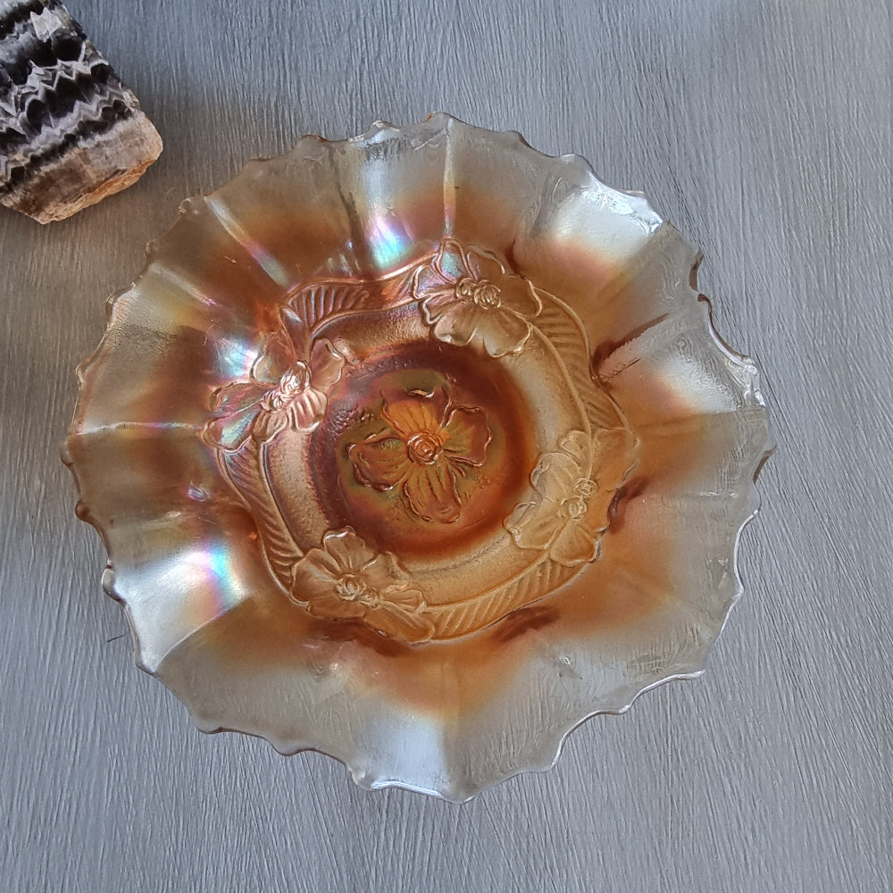 Vintage carnival glass bowl with ruffled edge and embossed floral pattern in peach-gold tones.