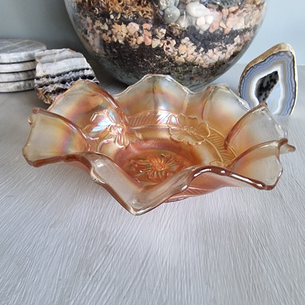 Vintage carnival glass bowl with ruffled edge and embossed floral pattern in peach-gold tones.