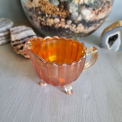 Amber carnival glass creamer jug with scalloped edge and three small feet.