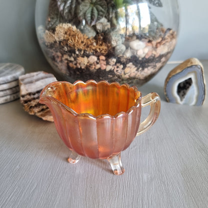 Amber carnival glass creamer jug with scalloped edge and three small feet.
