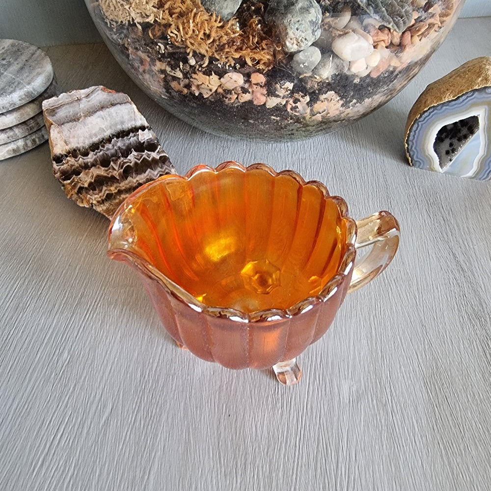 Amber carnival glass creamer jug with scalloped edge and three small feet.
