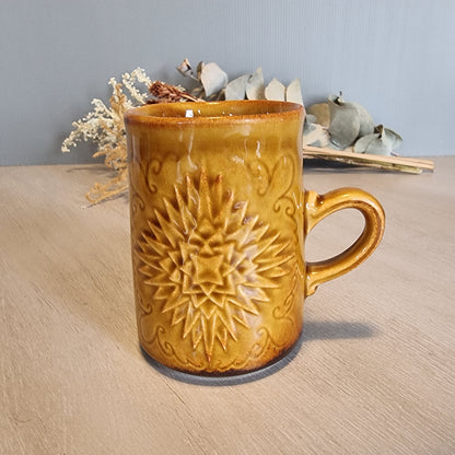 Crown Lynn mug with embossed starburst design in golden-brown glaze.