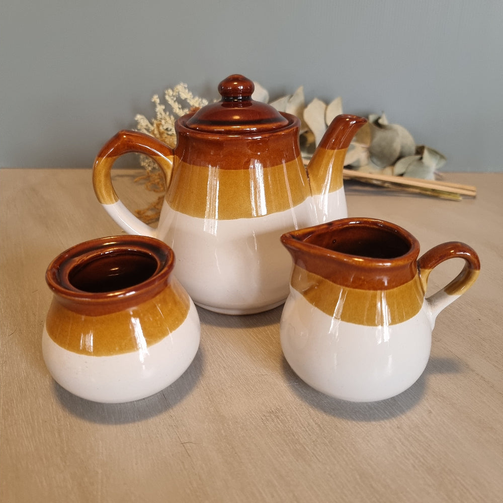 Three-piece vintage tea set in brown and mustard glaze with teapot, milk jug, and sugar bowl.