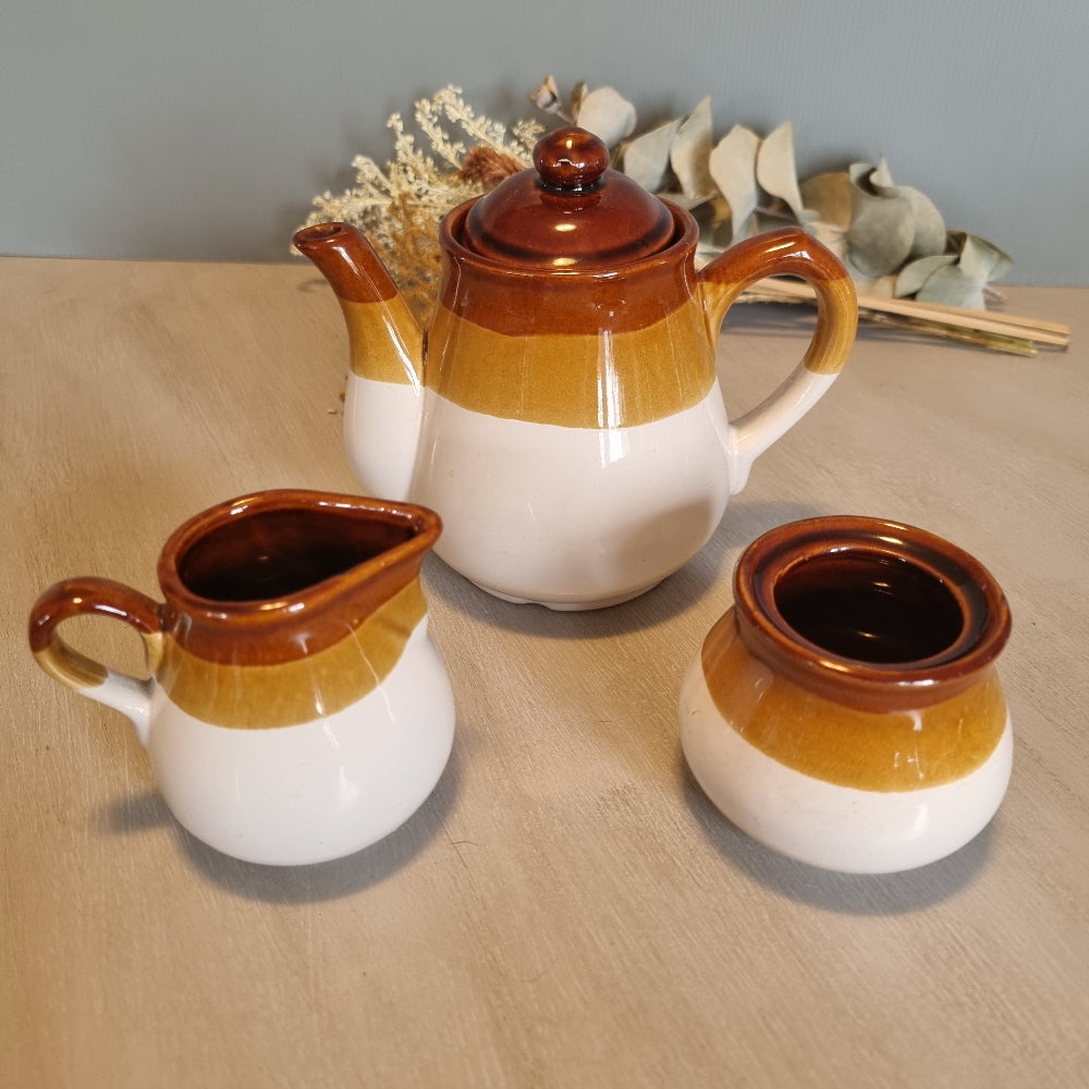 Three-piece vintage tea set in brown and mustard glaze with teapot, milk jug, and sugar bowl.