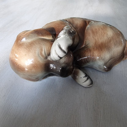 Vintage ceramic sleeping dog figurine in brown and cream glaze.