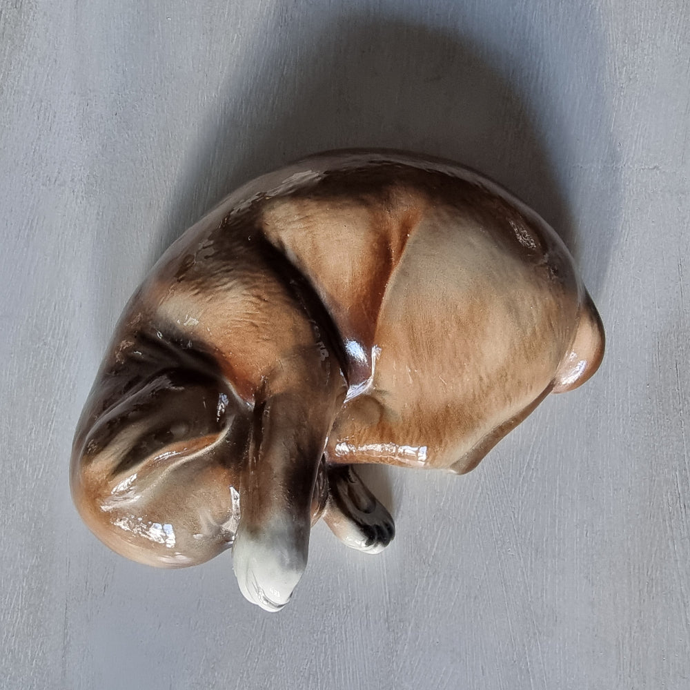 Vintage ceramic sleeping dog figurine in brown and cream glaze.