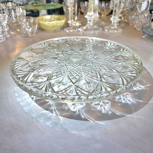 Clear pressed glass cake stand with starburst pattern and raised foot, catching light on a tabletop.