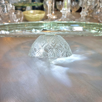 Clear pressed glass cake stand with starburst pattern and raised foot, catching light on a tabletop.