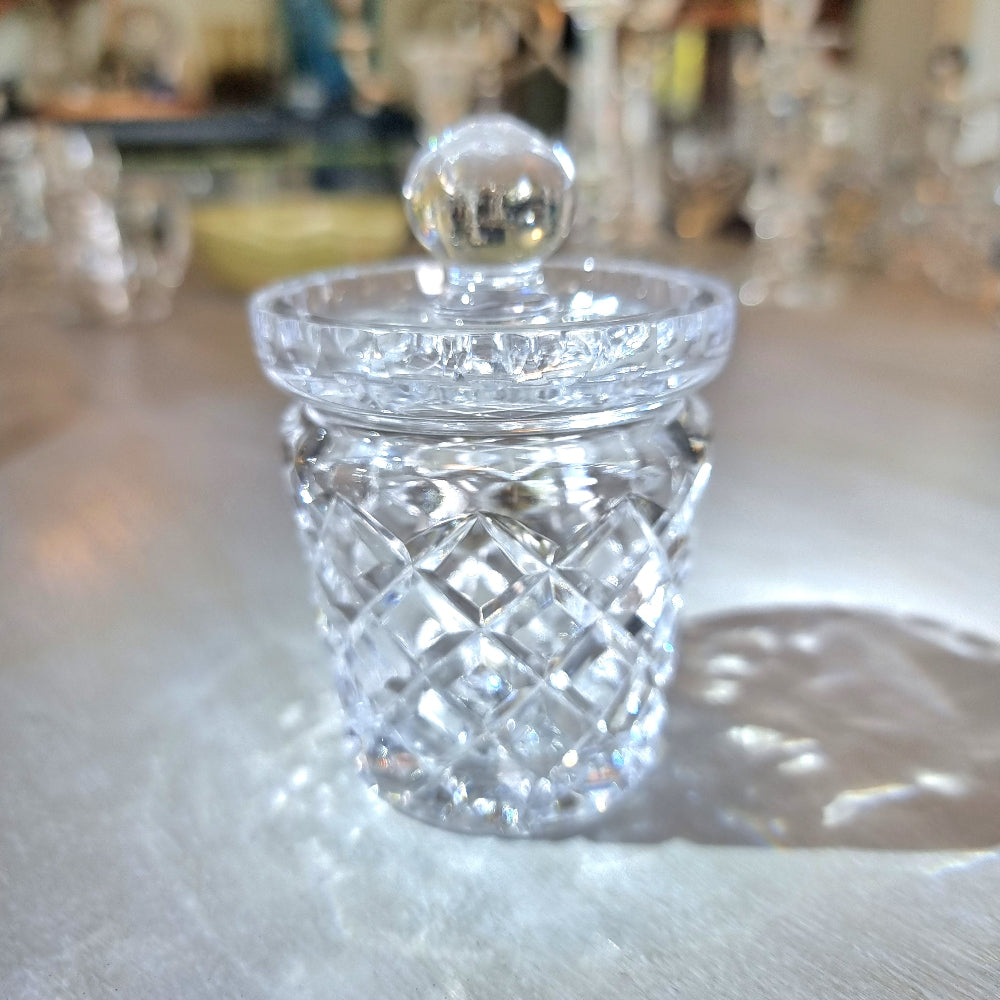 Small crystal jam jar with cut-glass lattice pattern and round lid knob catching the light.