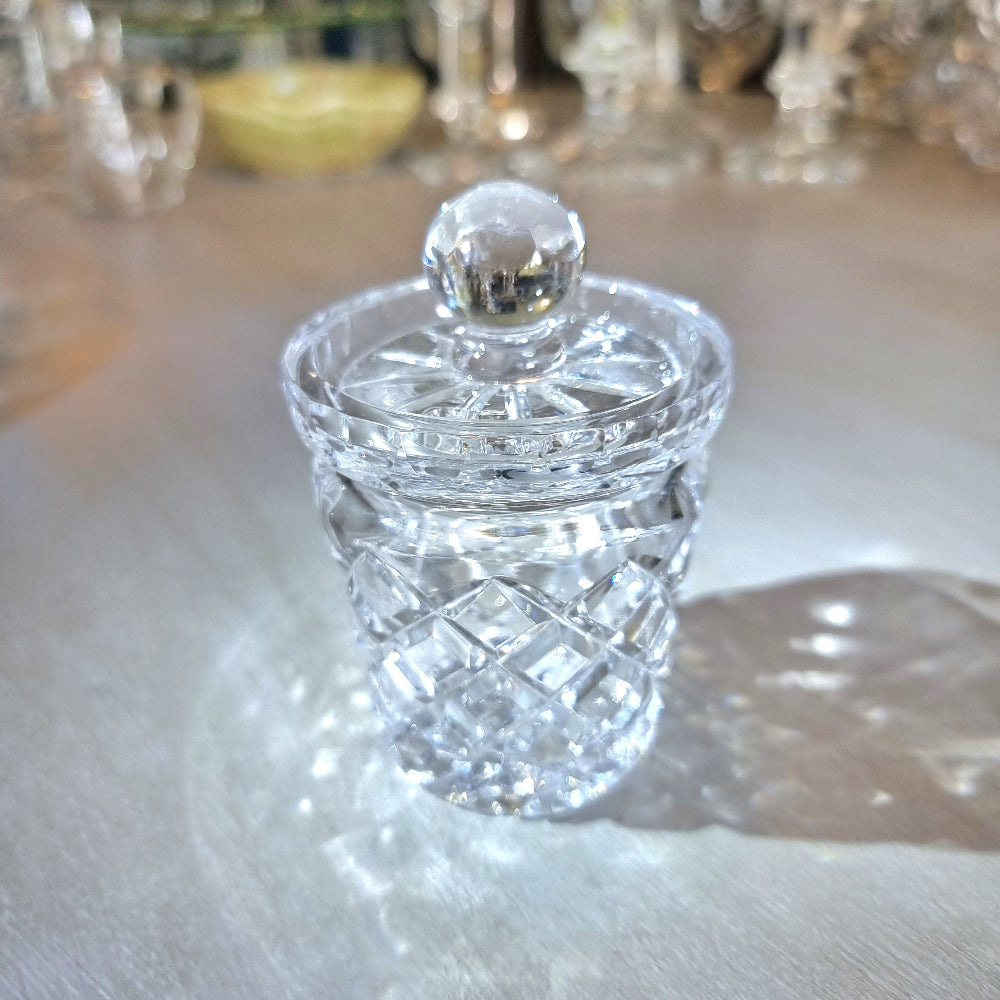 Small crystal jam jar with cut-glass lattice pattern and round lid knob catching the light.