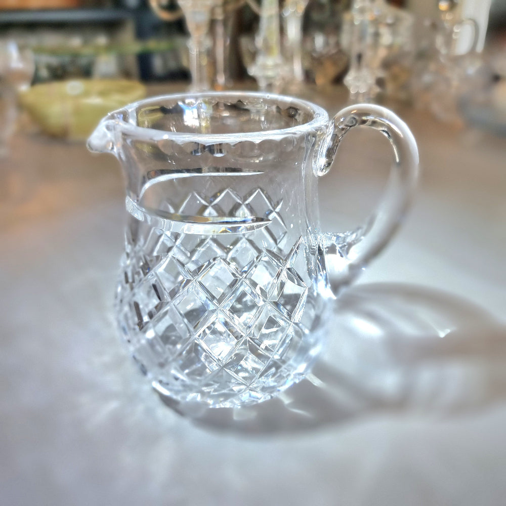 Heavy crystal jug with diamond-cut pattern and curved handle catching the light.