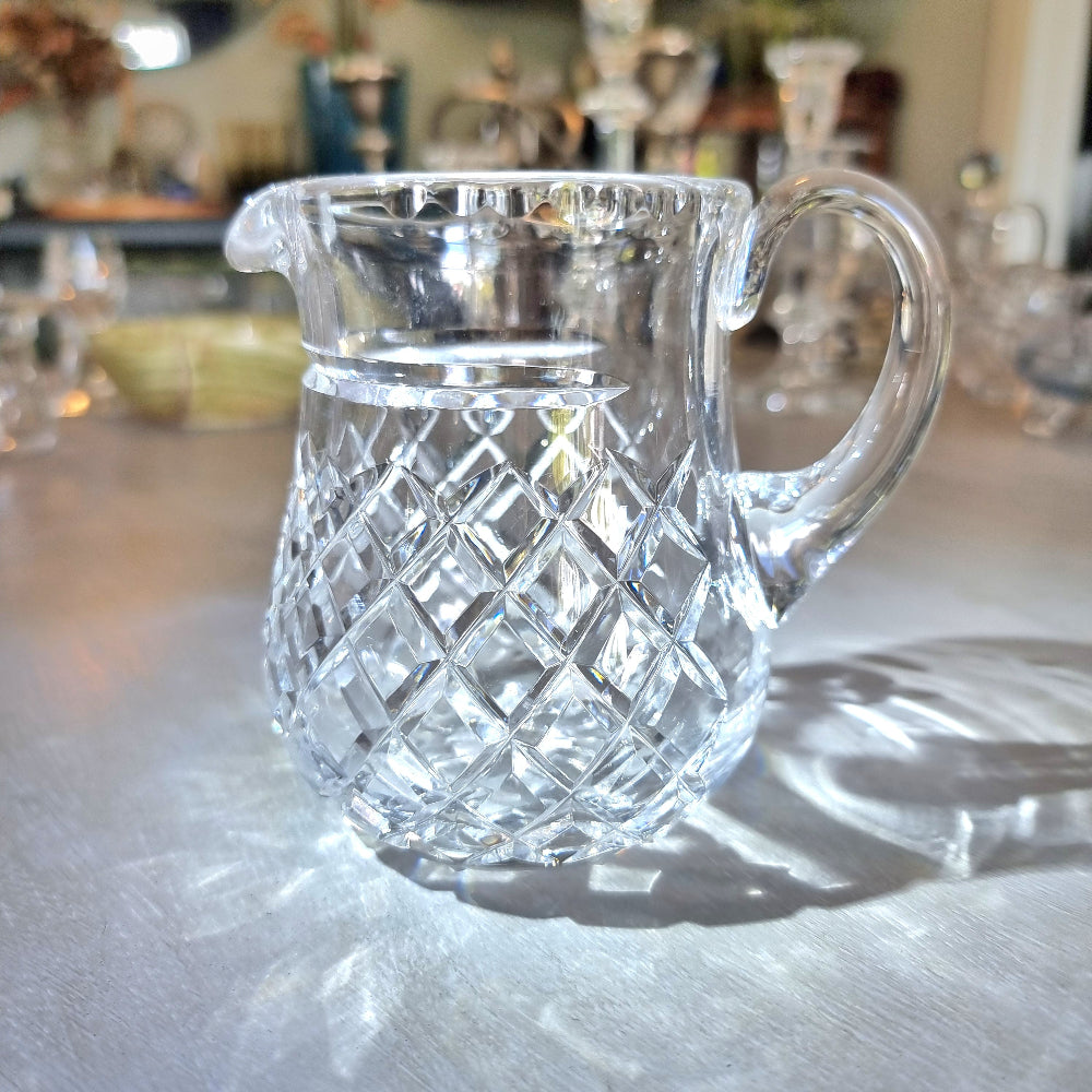 Heavy crystal jug with diamond-cut pattern and curved handle catching the light.