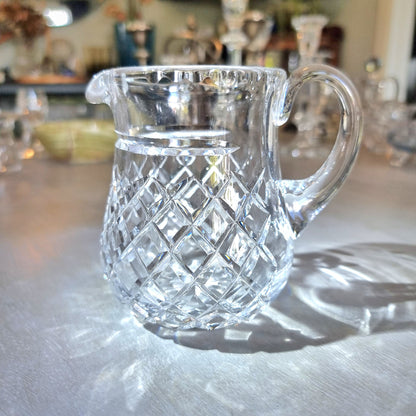 Heavy crystal jug with diamond-cut pattern and curved handle catching the light.