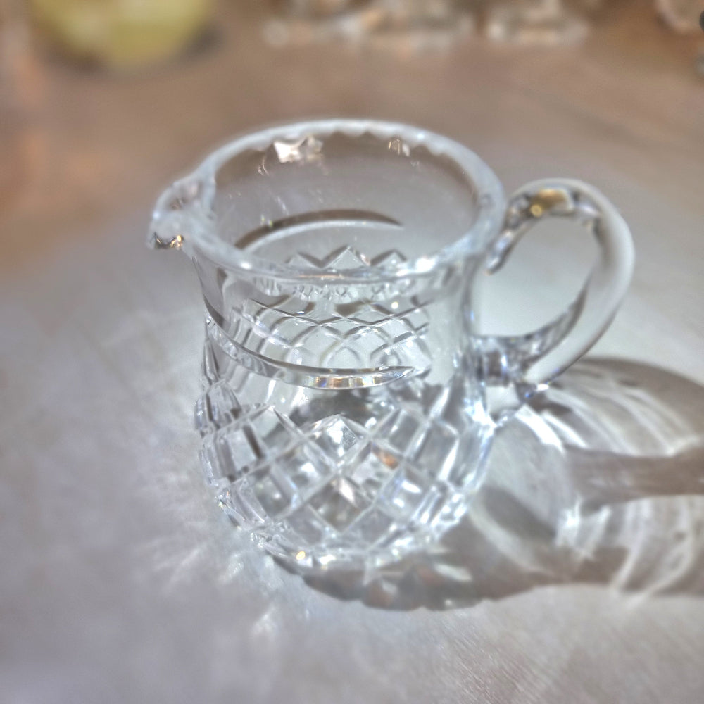 Heavy crystal jug with diamond-cut pattern and curved handle catching the light.