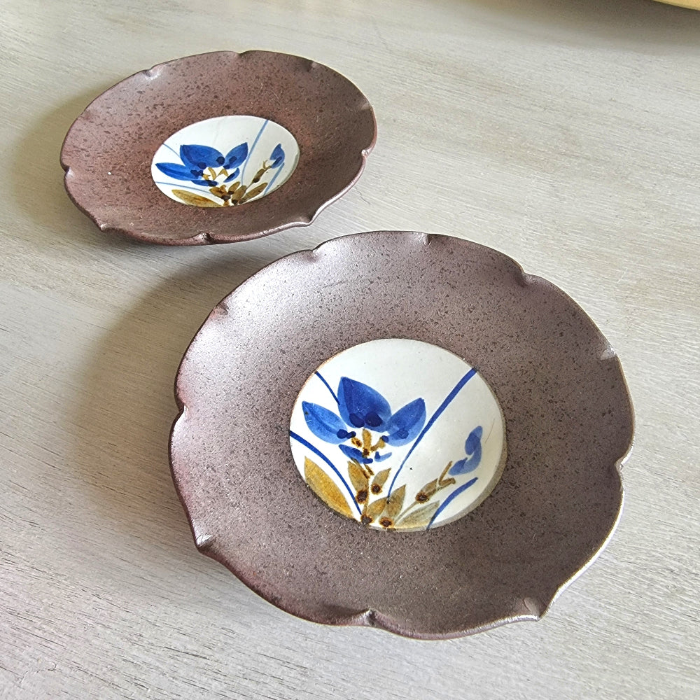 Pair of ceramic dishes with blue floral centres and speckled mauve scalloped rims.