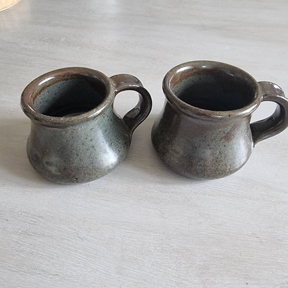 Pair of rustic earthenware mugs with green-brown glaze and rounded shape.