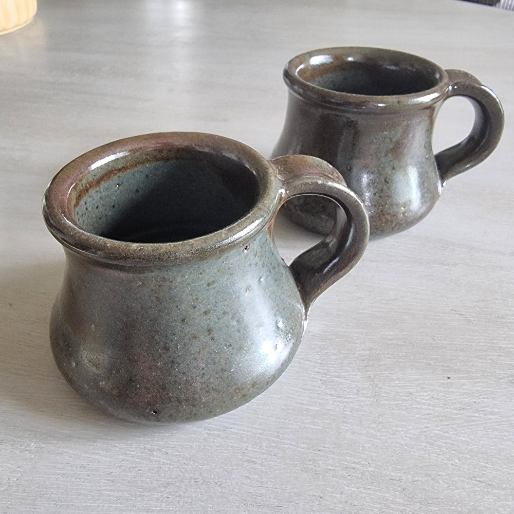 Pair of rustic earthenware mugs with green-brown glaze and rounded shape.