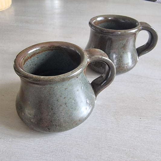 Pair of rustic earthenware mugs with green-brown glaze and rounded shape.