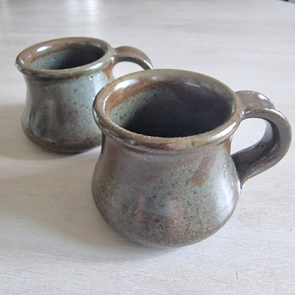 Pair of rustic earthenware mugs with green-brown glaze and rounded shape.