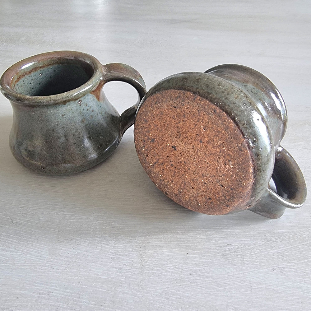 Pair of rustic earthenware mugs with green-brown glaze and rounded shape.