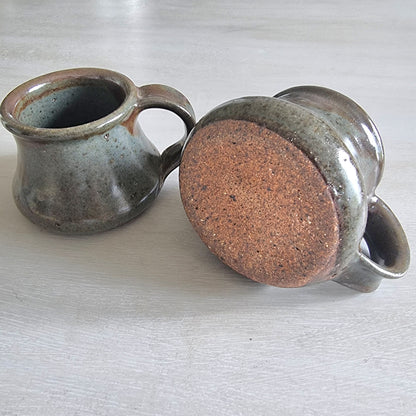 Pair of rustic earthenware mugs with green-brown glaze and rounded shape.