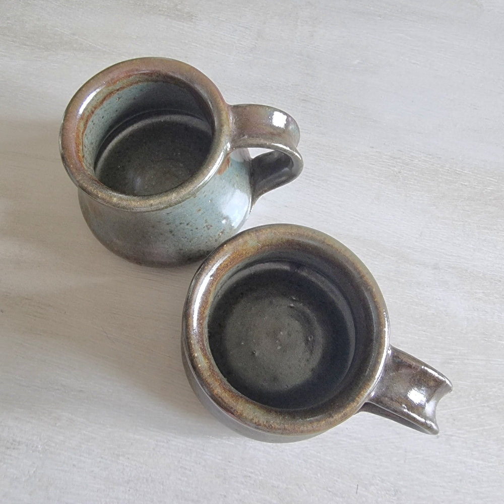 Pair of rustic earthenware mugs with green-brown glaze and rounded shape.