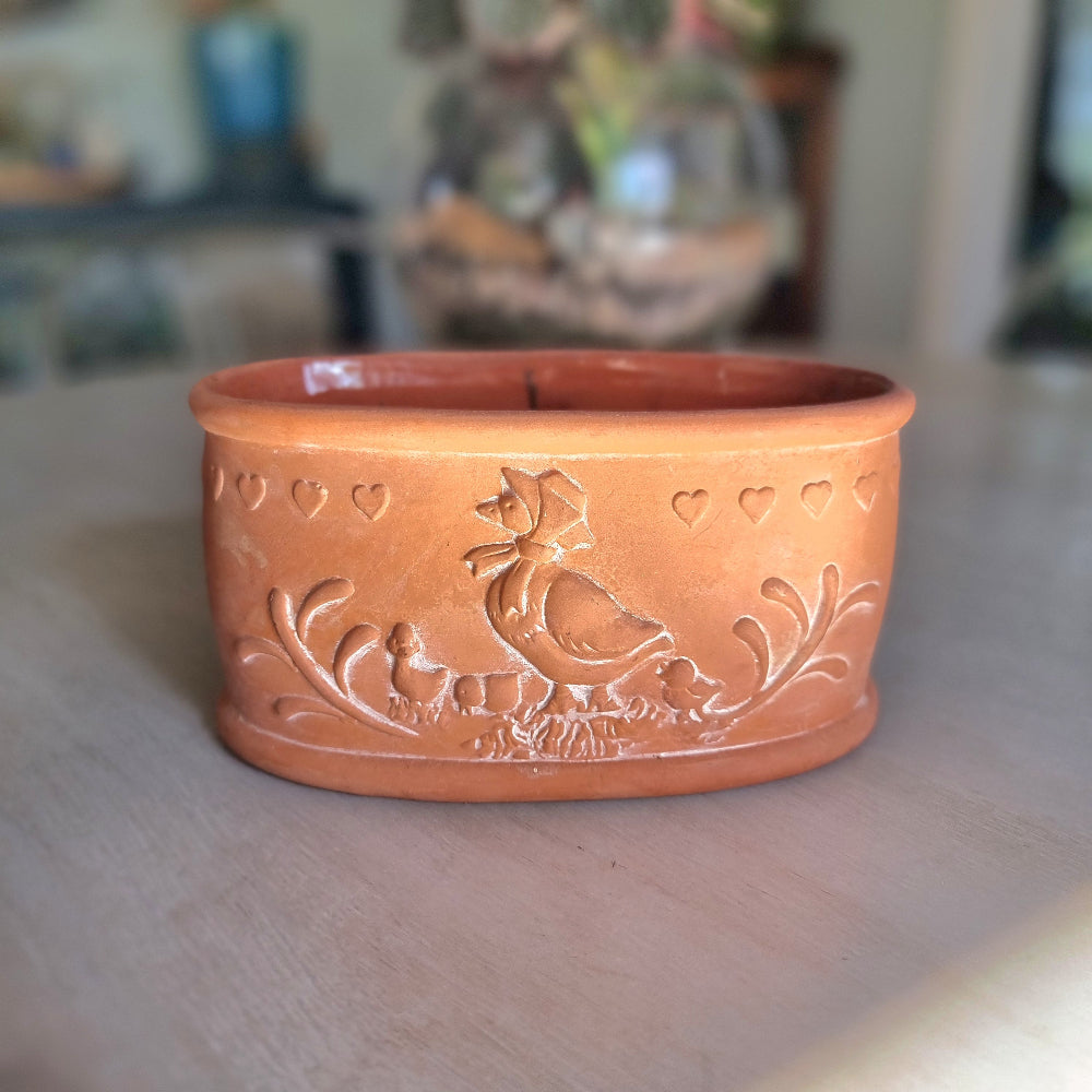 Terracotta ceramic bowl with embossed hen, chicks and heart details, photographed on a tabletop.
