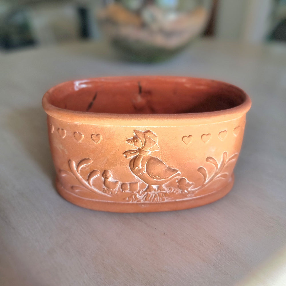 Terracotta ceramic bowl with embossed hen, chicks and heart details, photographed on a tabletop.