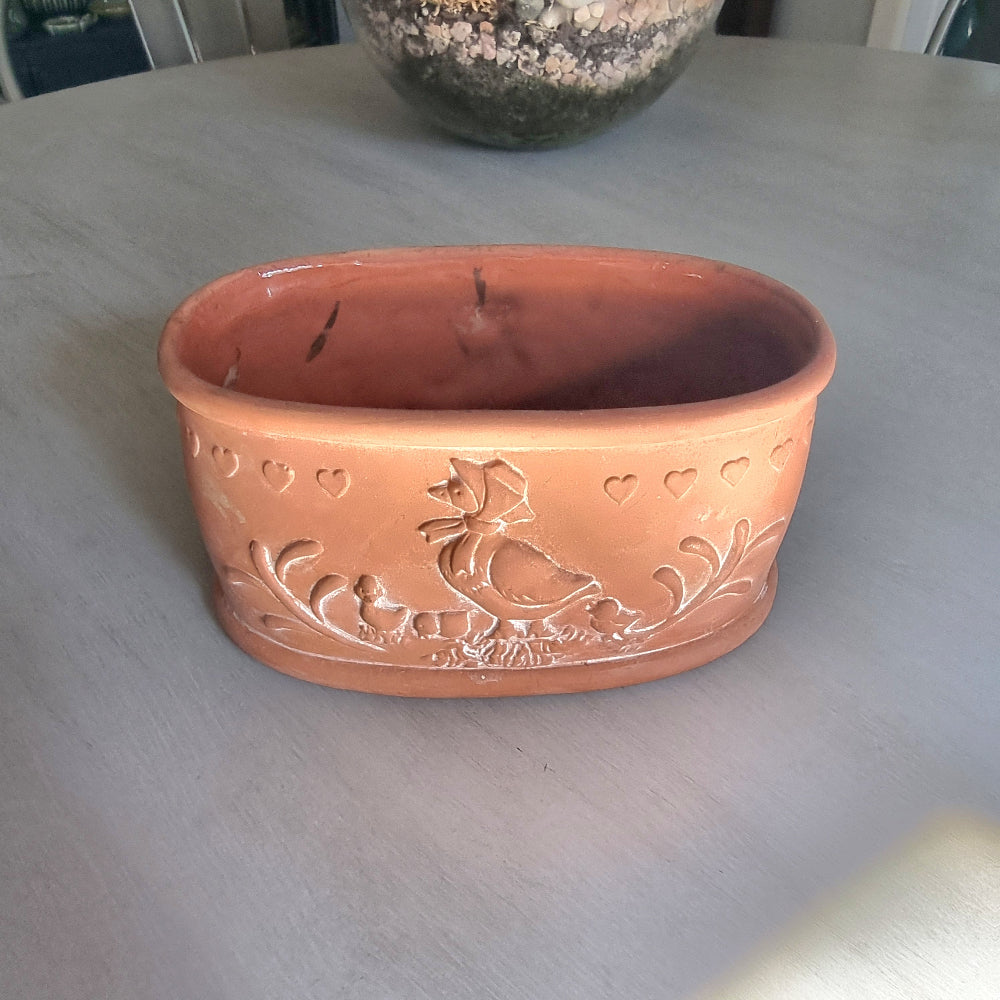 Terracotta ceramic bowl with embossed hen, chicks and heart details, photographed on a tabletop.