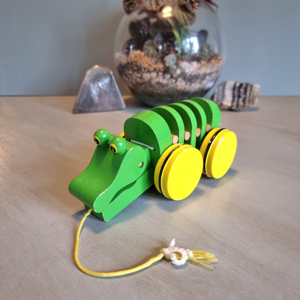 Vintage green wooden pull-along crocodile toy with yellow wheels.