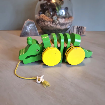 Vintage green wooden pull-along crocodile toy with yellow wheels.