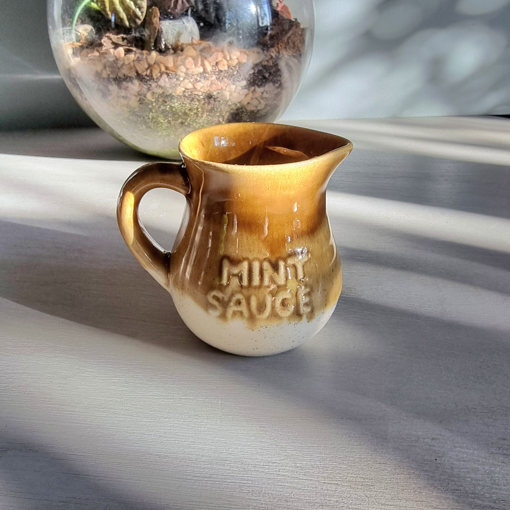 Vintage ceramic mint sauce jug with raised lettering and warm caramel and cream glaze on a tabletop.