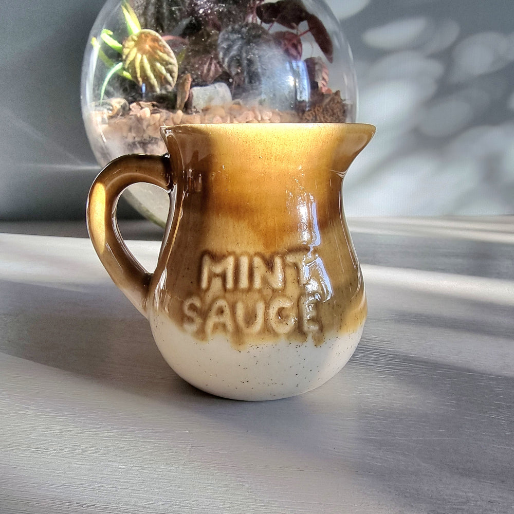Vintage ceramic mint sauce jug with raised lettering and warm caramel and cream glaze on a tabletop.