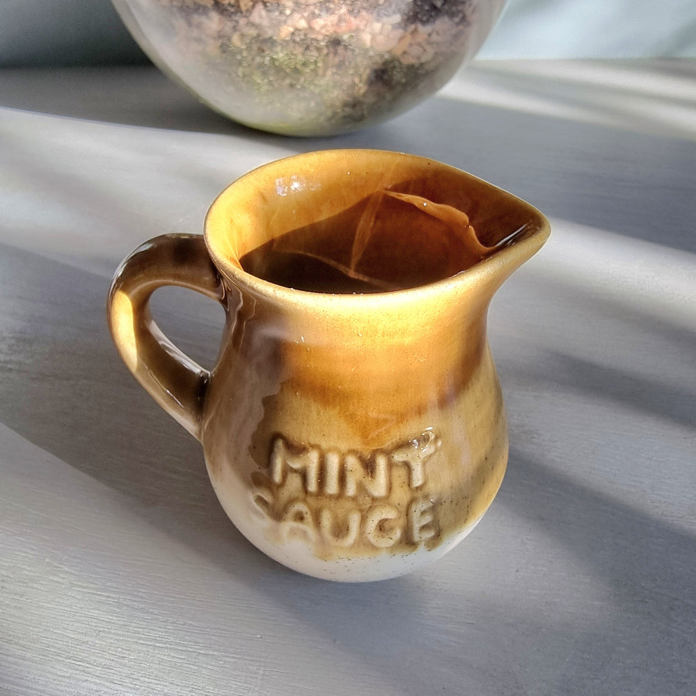 Vintage ceramic mint sauce jug with raised lettering and warm caramel and cream glaze on a tabletop.