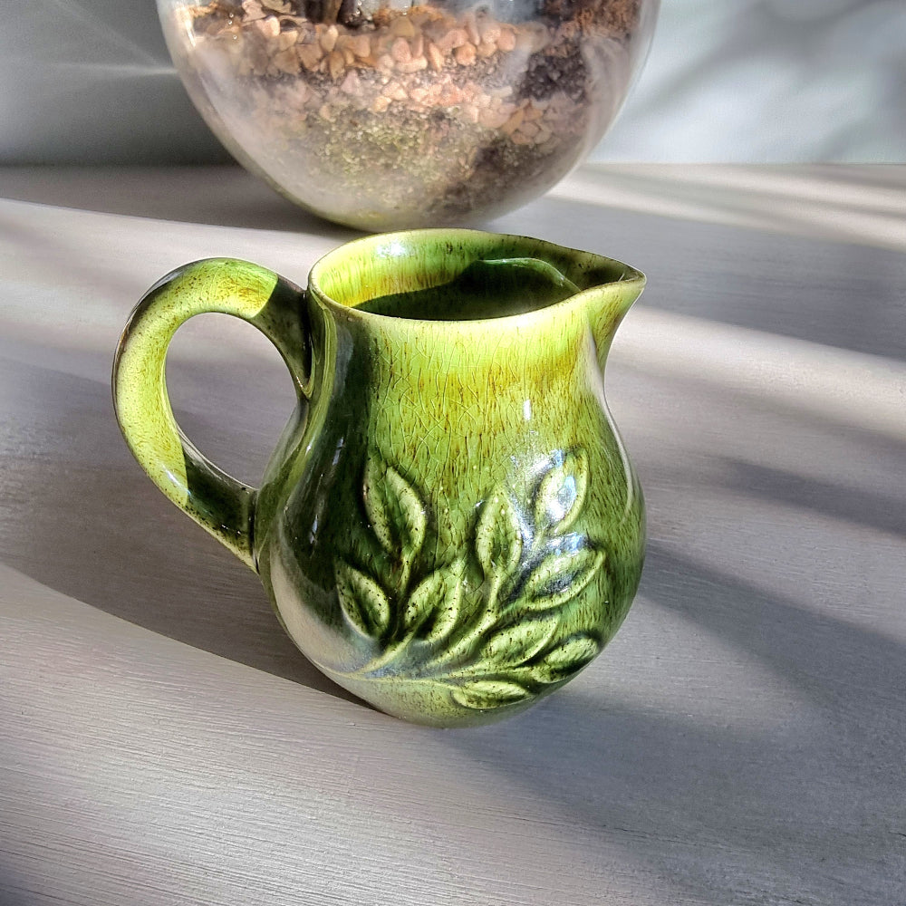 Vintage Holkham green ceramic cream jug with crackle glaze and raised leaf pattern on a tabletop.