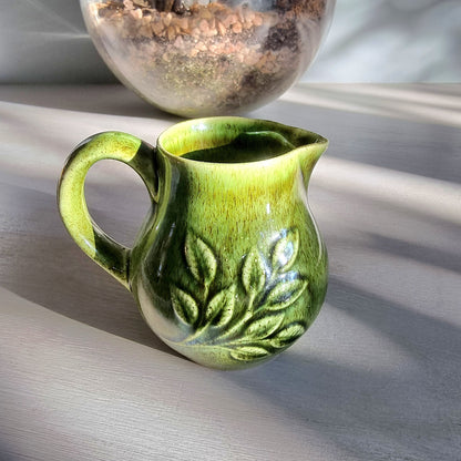 Vintage Holkham green ceramic cream jug with crackle glaze and raised leaf pattern on a tabletop.