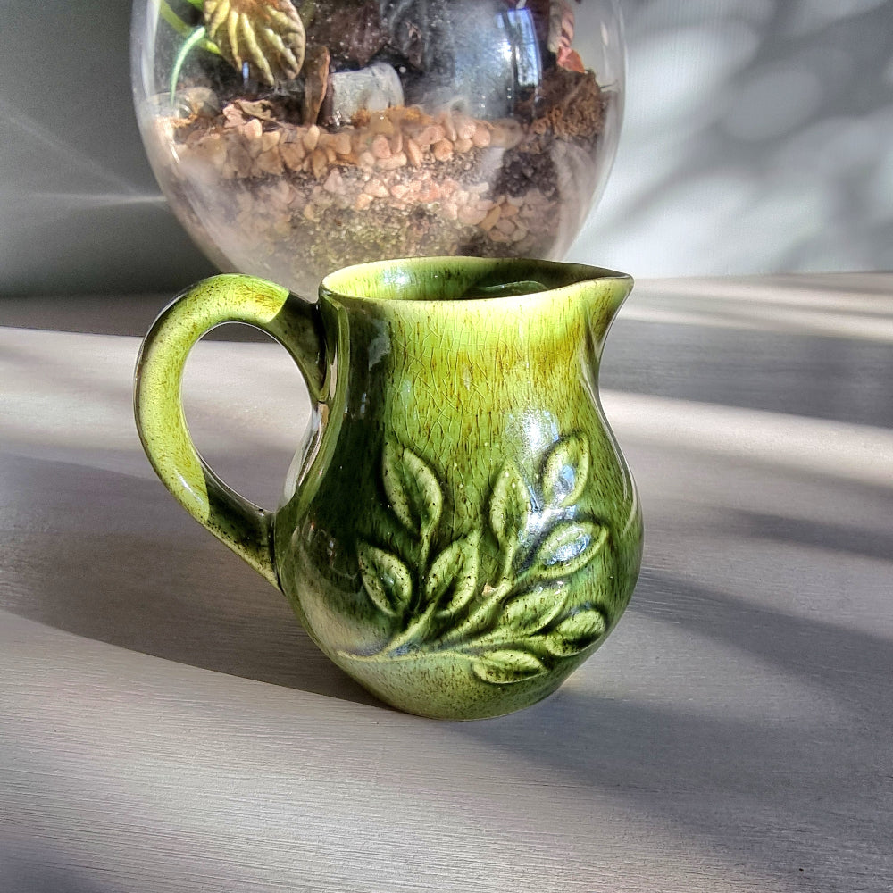 Vintage Holkham green ceramic cream jug with crackle glaze and raised leaf pattern on a tabletop.