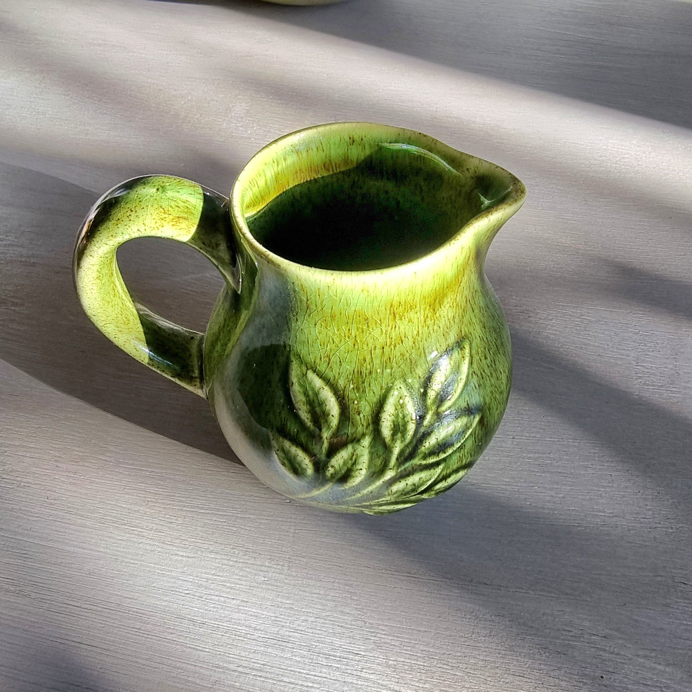 Vintage Holkham green ceramic cream jug with crackle glaze and raised leaf pattern on a tabletop.