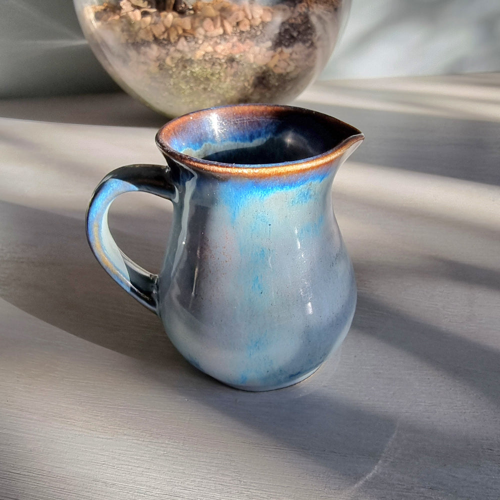 Vintage Clay Craft cream jug with blue reactive glaze and stamped base, styled on a tabletop.