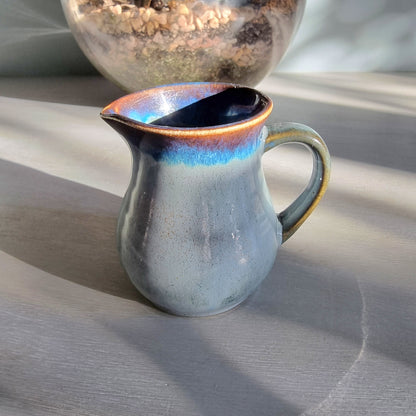 Vintage Clay Craft cream jug with blue reactive glaze and stamped base, styled on a tabletop.