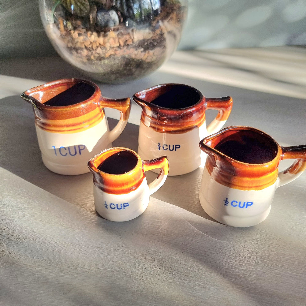 Vintage ceramic measuring jug set with caramel glaze and blue cup markings, including one cracked jug, styled on a table.
